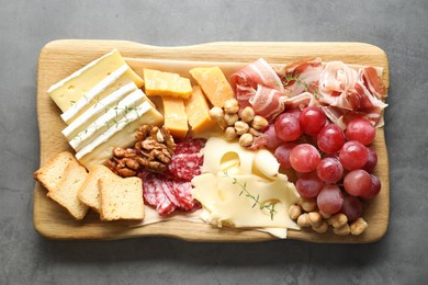 Photo of Different types of cut cheese and other snacks on gray textured table, top view