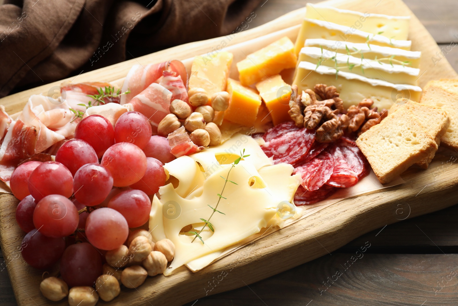 Photo of Different types of cut cheese and other snacks on wooden table, closeup