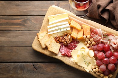 Photo of Different types of cut cheese and other snacks served with wine on wooden table, flat lay. Space for text