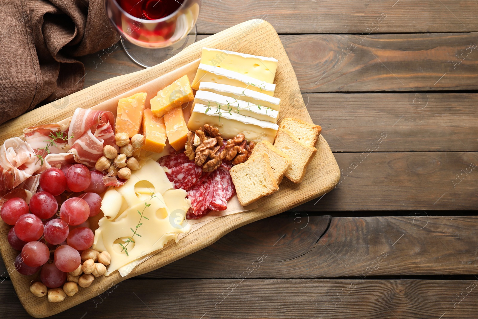 Photo of Different types of cut cheese and other snacks served with wine on wooden table, flat lay. Space for text