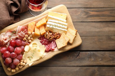 Photo of Different types of cut cheese and other snacks served with wine on wooden table, flat lay. Space for text