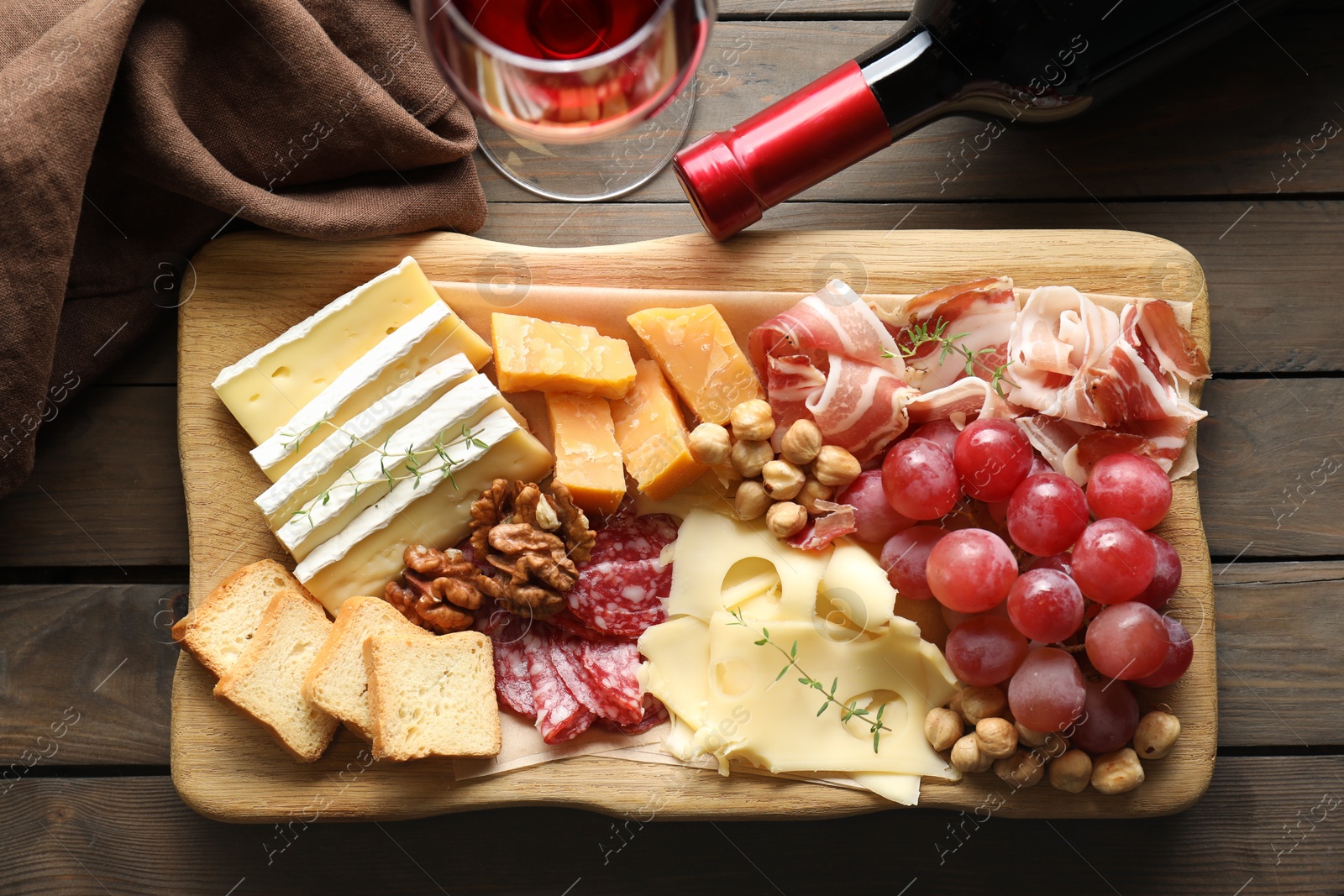 Photo of Different types of cut cheese and other snacks served with wine on wooden table, flat lay