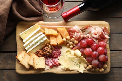 Photo of Different types of cut cheese and other snacks served with wine on wooden table, flat lay