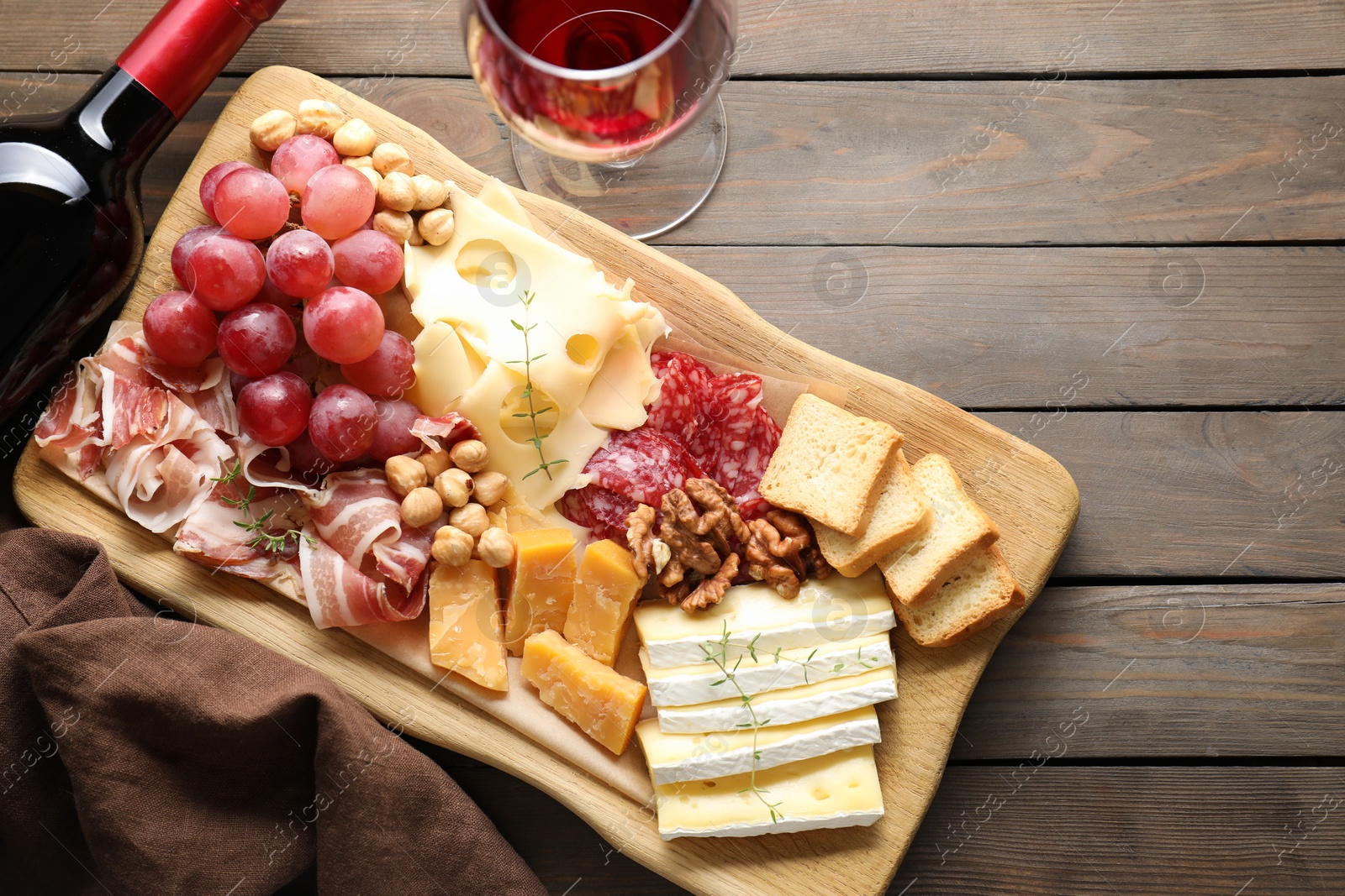 Photo of Different types of cut cheese and other snacks served with wine on wooden table, flat lay. Space for text