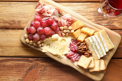 Photo of Different types of cut cheese and other snacks served with wine on wooden table, flat lay