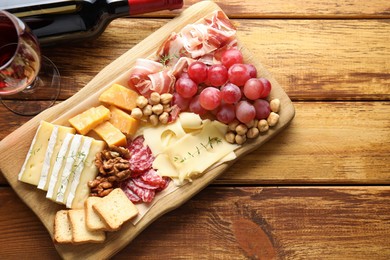 Photo of Different types of cut cheese and other snacks served with wine on wooden table, flat lay. Space for text