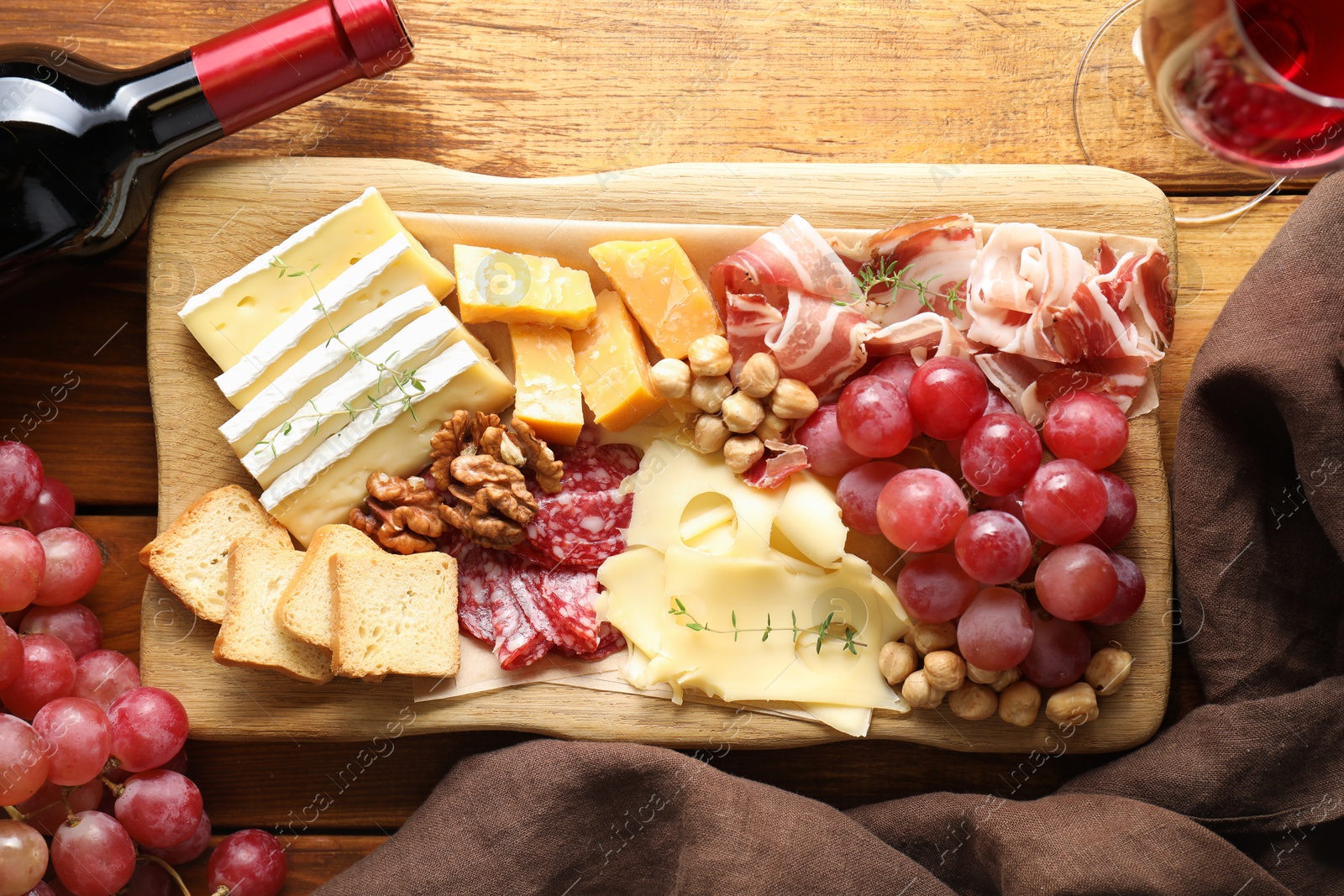 Photo of Different types of cut cheese and other snacks served with wine on wooden table, flat lay