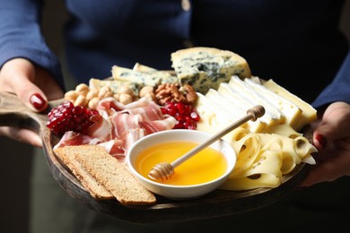 Photo of Woman holding board with different types of delicious cheese and other snacks, closeup