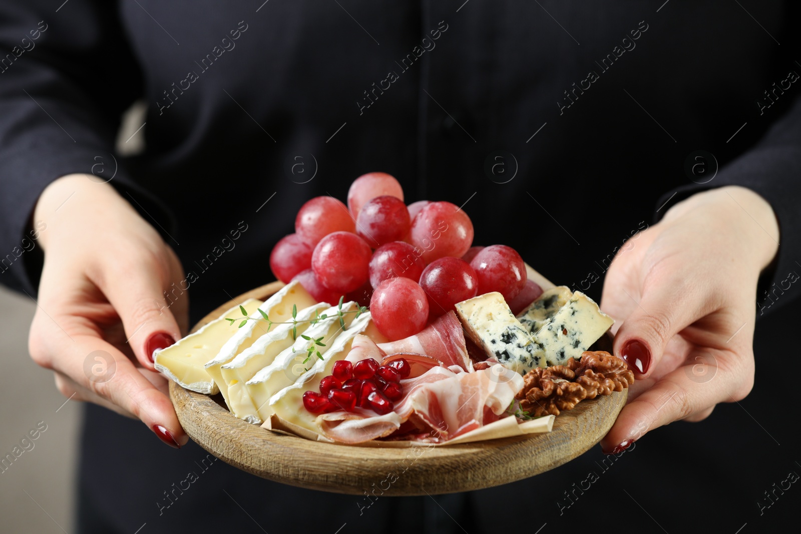 Photo of Woman holding board with different types of delicious cheese and other snacks, closeup