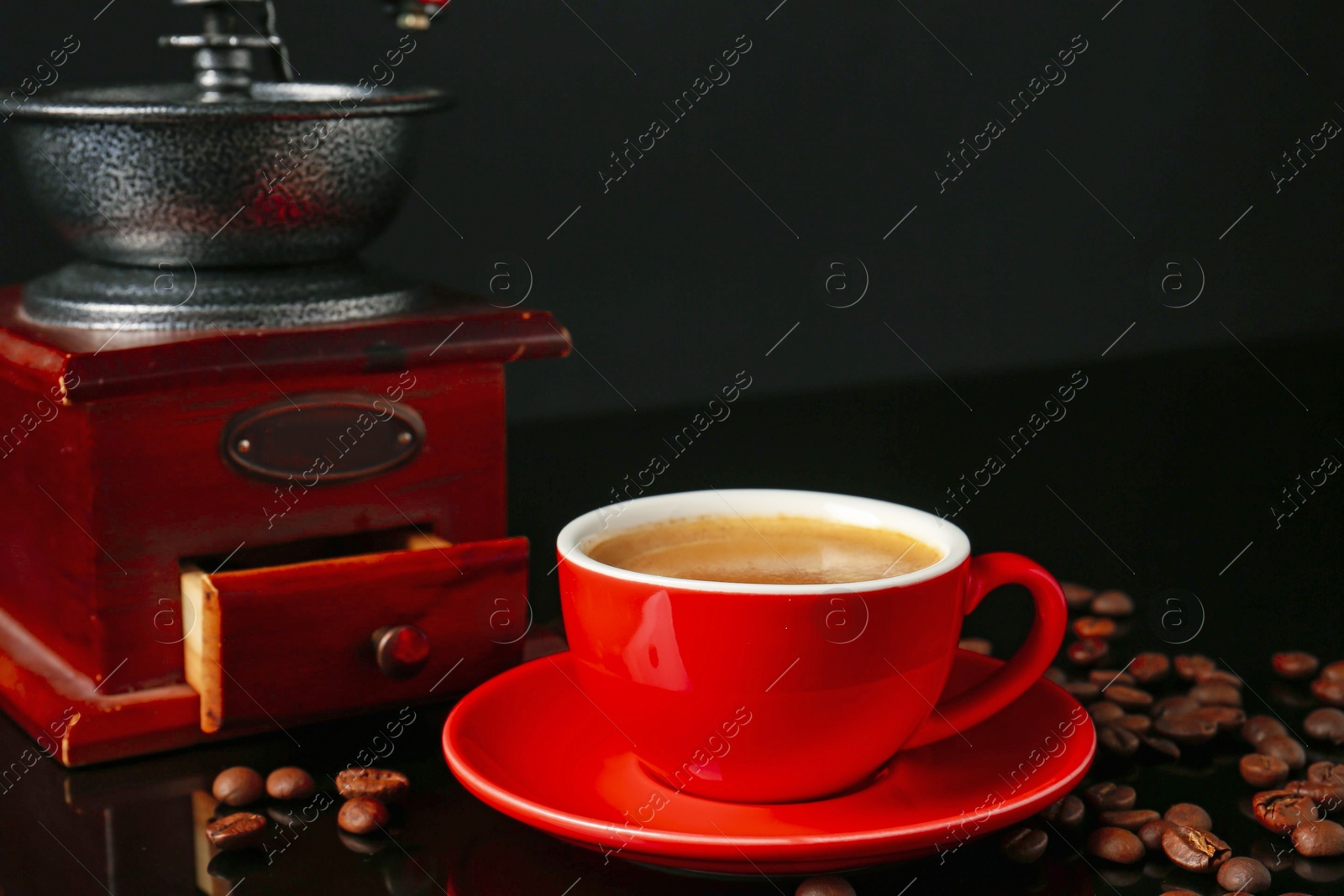 Red cup with coffee, roasted beans and vintage grinder on black background Photo of Red cup with coffee, roasted beans and vintage grinder on black background
