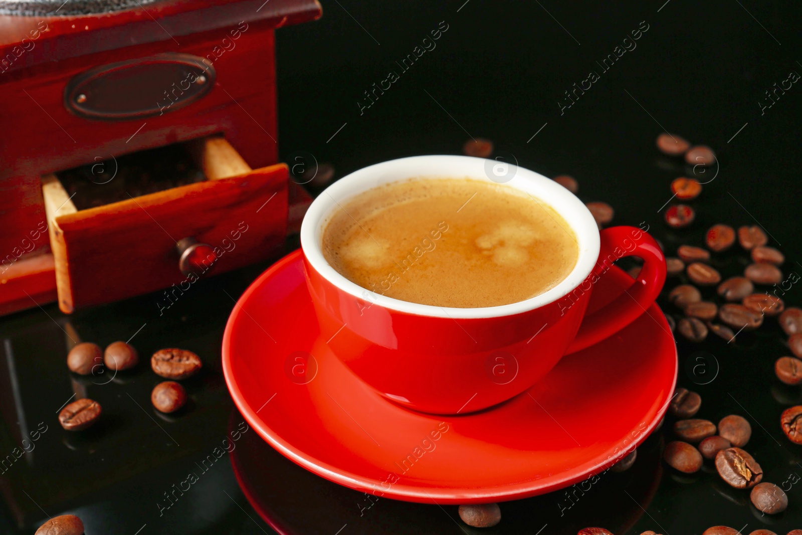 Red cup with coffee, roasted beans and vintage grinder on black background Photo of Red cup with coffee, roasted beans and vintage grinder on black background