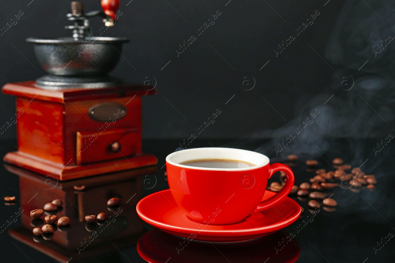 Red cup with coffee, vintage grinder and roasted beans on black background Photo of Red cup with coffee, vintage grinder and roasted beans on black background