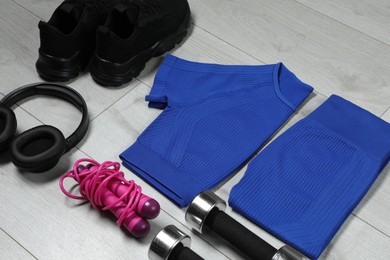 Photo of Stylish sportswear, black sneakers, dumbbells, skipping rope and headphones on wooden background, closeup