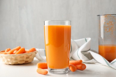 Photo of Fresh carrot juice in glass and vegetables on white table against gray background