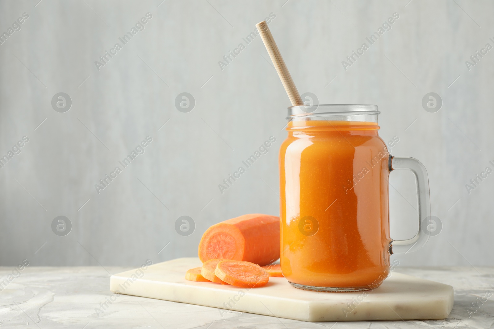 Photo of Fresh carrot juice in mason jar and vegetable on gray textured table, space for text