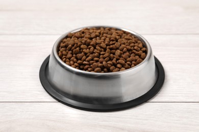 Photo of Dry pet food granules in feeding bowl on floor