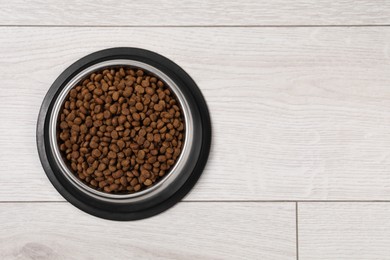 Photo of Dry pet food granules in feeding bowl on floor, top view. Space for text