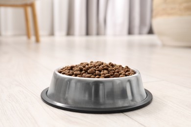 Photo of Dry pet food granules in feeding bowl on floor indoors