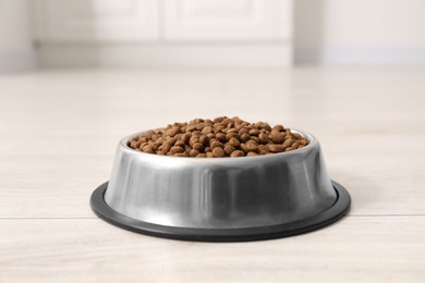 Photo of Dry pet food granules in feeding bowl on floor indoors