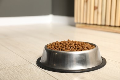 Photo of Dry pet food granules in feeding bowl on floor indoors, space for text