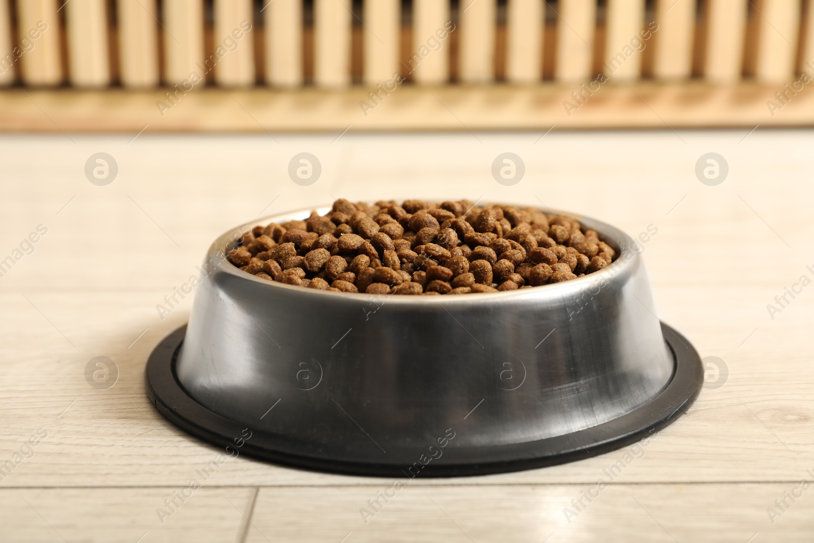 Photo of Dry pet food granules in feeding bowl on floor indoors