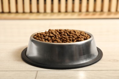 Dry pet food granules in feeding bowl on floor indoors