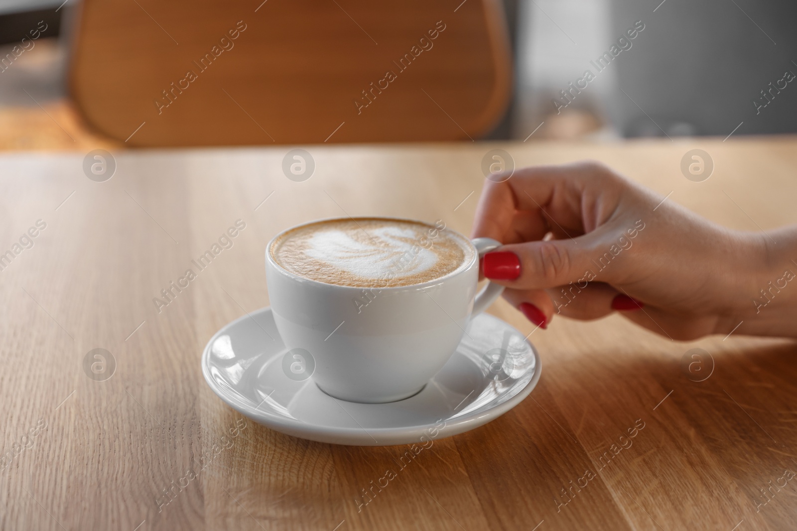 Photo of Woman with cup of aromatic coffee at wooden table in cafe, closeup