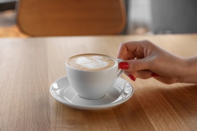 Photo of Woman with cup of aromatic coffee at wooden table in cafe, closeup