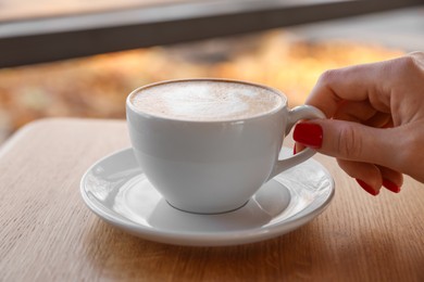 Photo of Woman with cup of aromatic coffee at wooden table in cafe, closeup