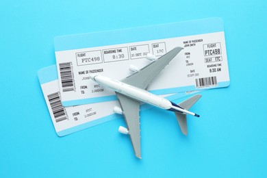 Photo of Travel agency. Flight tickets and plane model on light blue background, flat lay