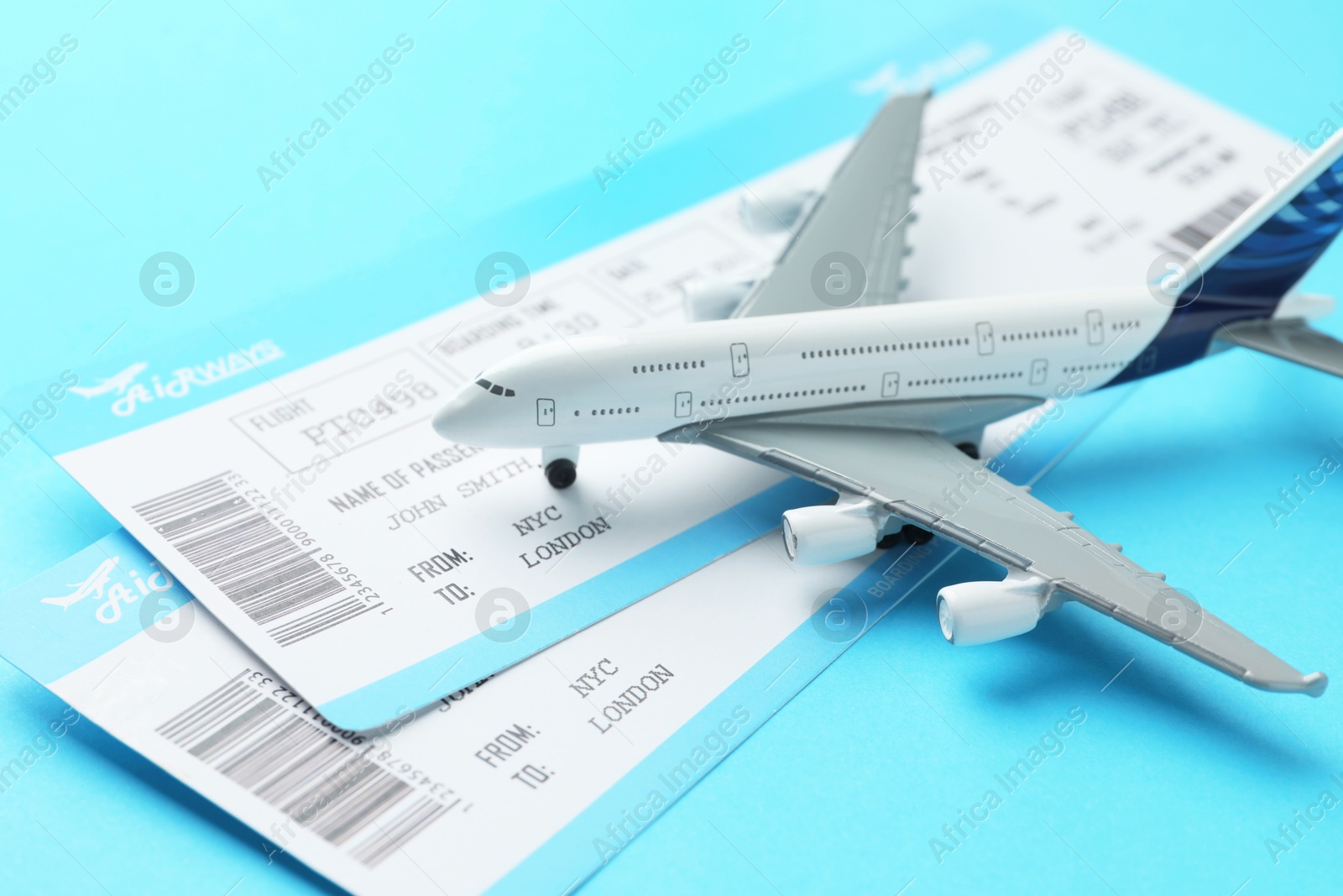 Photo of Travel agency. Flight tickets and plane model on light blue background, closeup