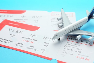 Photo of Travel agency. Flight tickets and plane model on light blue background, closeup