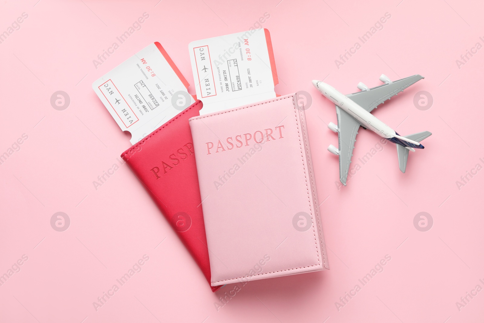 Photo of Travel agency. Flight tickets, passports and plane model on pink background, top view