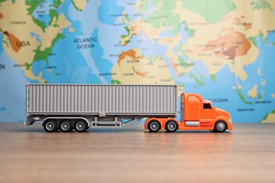 Photo of Toy truck on wooden table against world map. Logistics concept