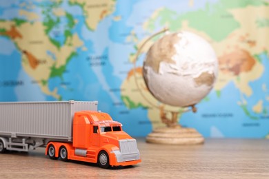 Photo of Toy truck and globe on wooden table against world map, closeup. Logistics concept