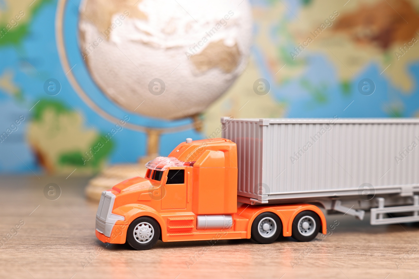 Photo of Toy truck and globe on wooden table against world map, closeup. Logistics concept