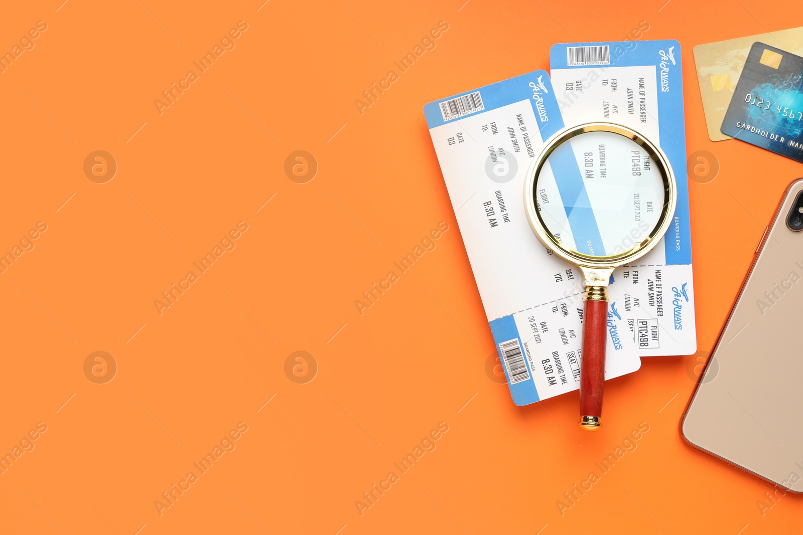 Photo of Travel agency. Flight tickets, magnifying glass, credit cards and smartphone on orange background, flat lay. Space for text