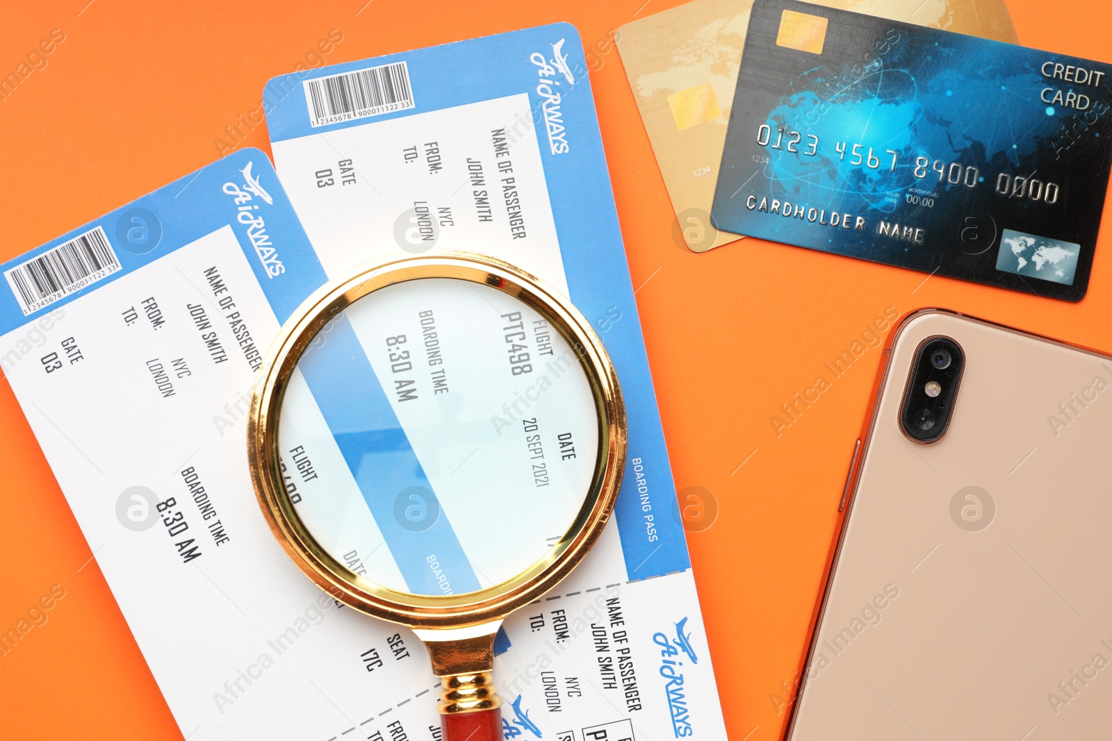 Photo of Travel agency. Flight tickets, magnifying glass, credit cards and smartphone on orange background, flat lay