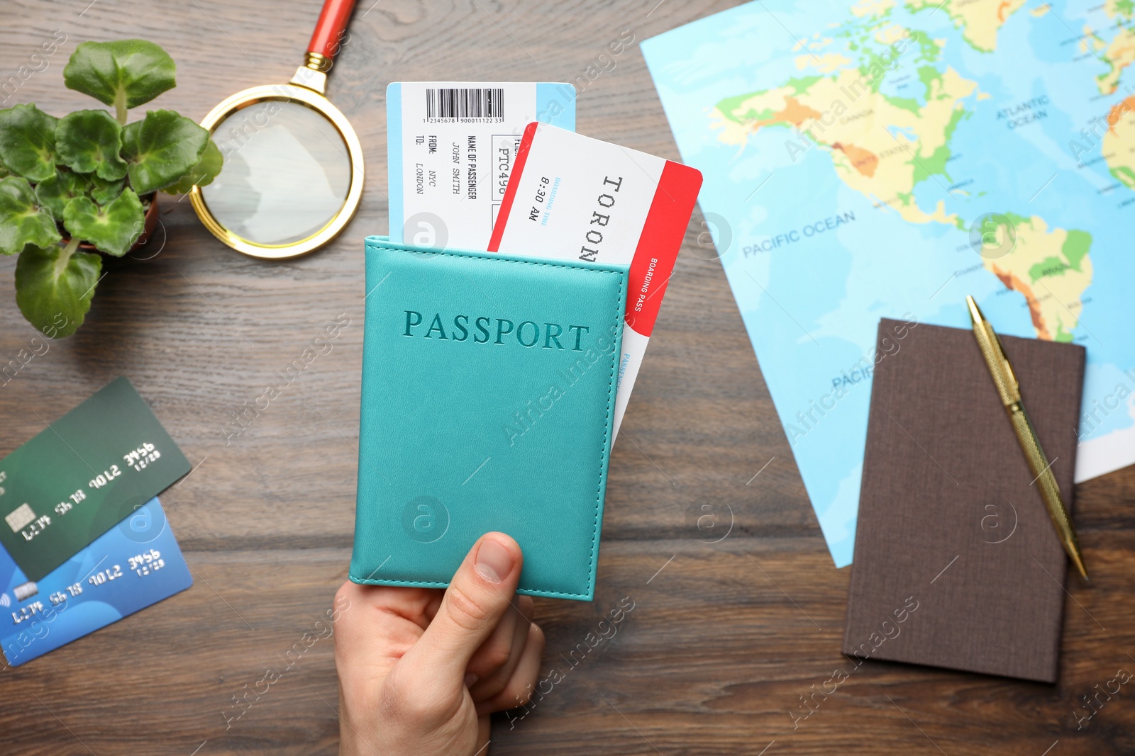 Photo of Travel agency. Man holding passport with flight tickets at wooden table, top view