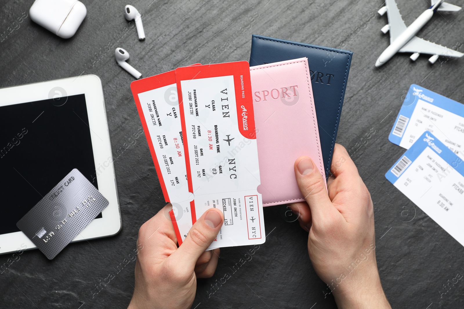 Photo of Travel agency. Man holding passports and flight tickets at dark textured table, top view