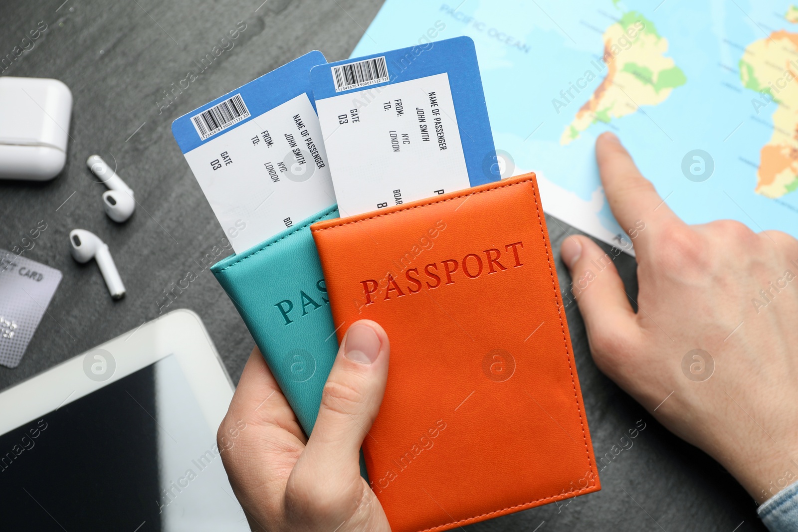 Photo of Travel agency. Man with passports and flight tickets pointing at destination on map at dark textured table, top view