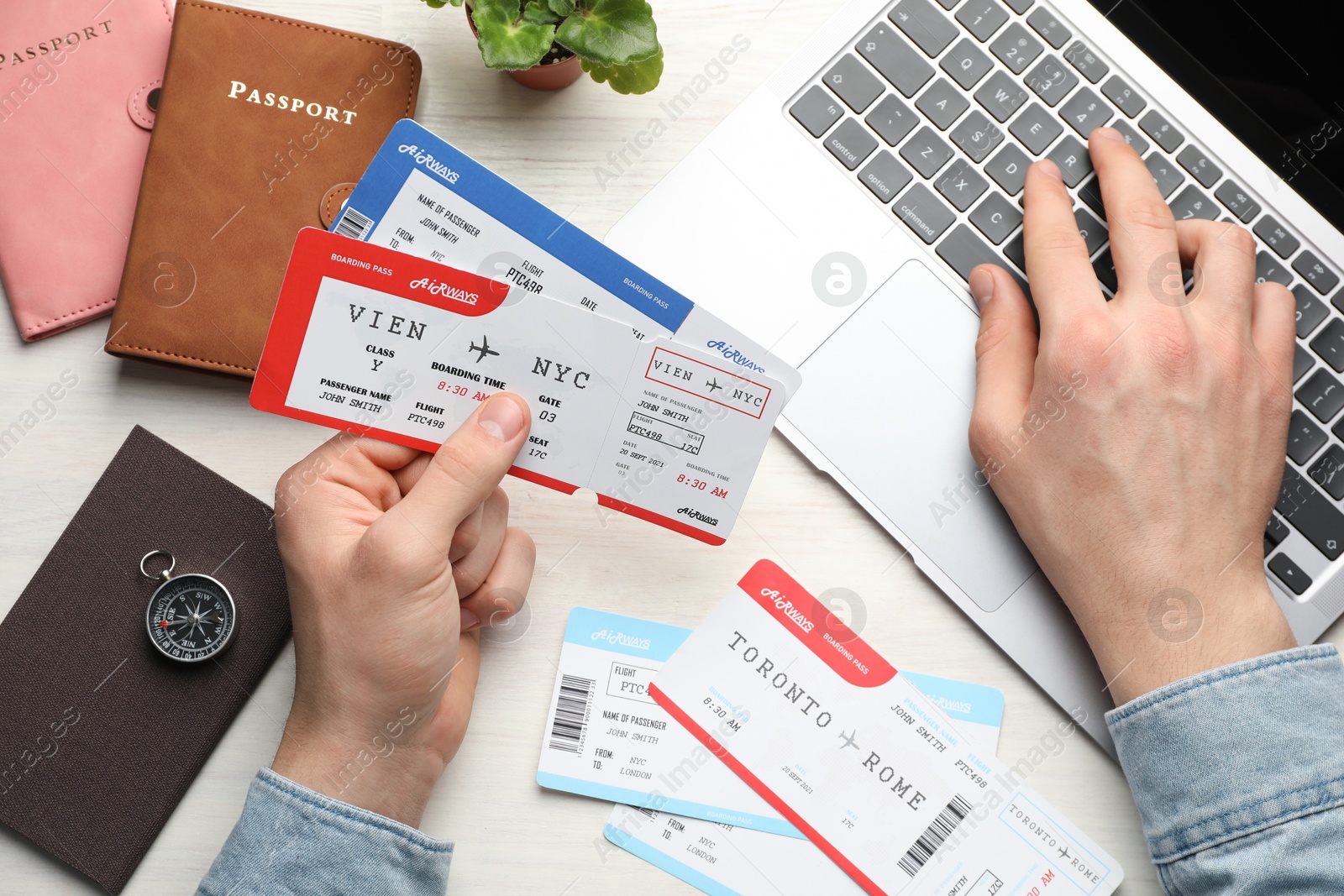 Photo of Travel agency. Man with flight tickets using laptop at light wooden table, top view