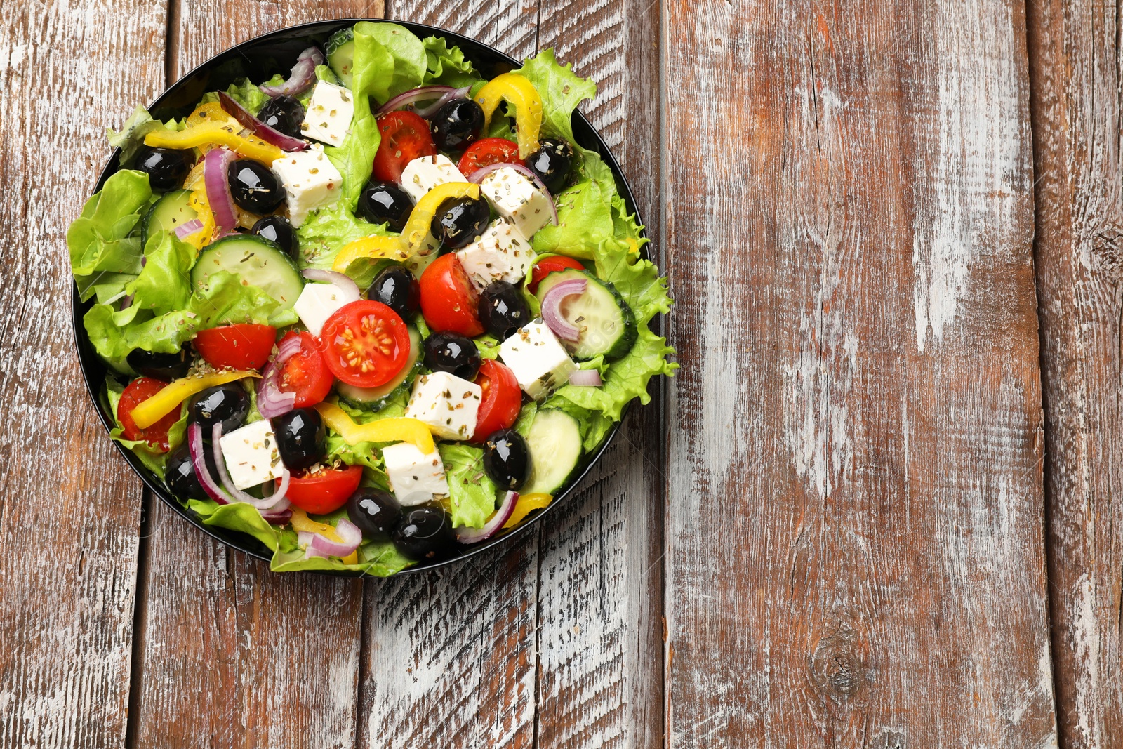 Photo of Delicious fresh Greek salad on wooden table, top view. Space for text