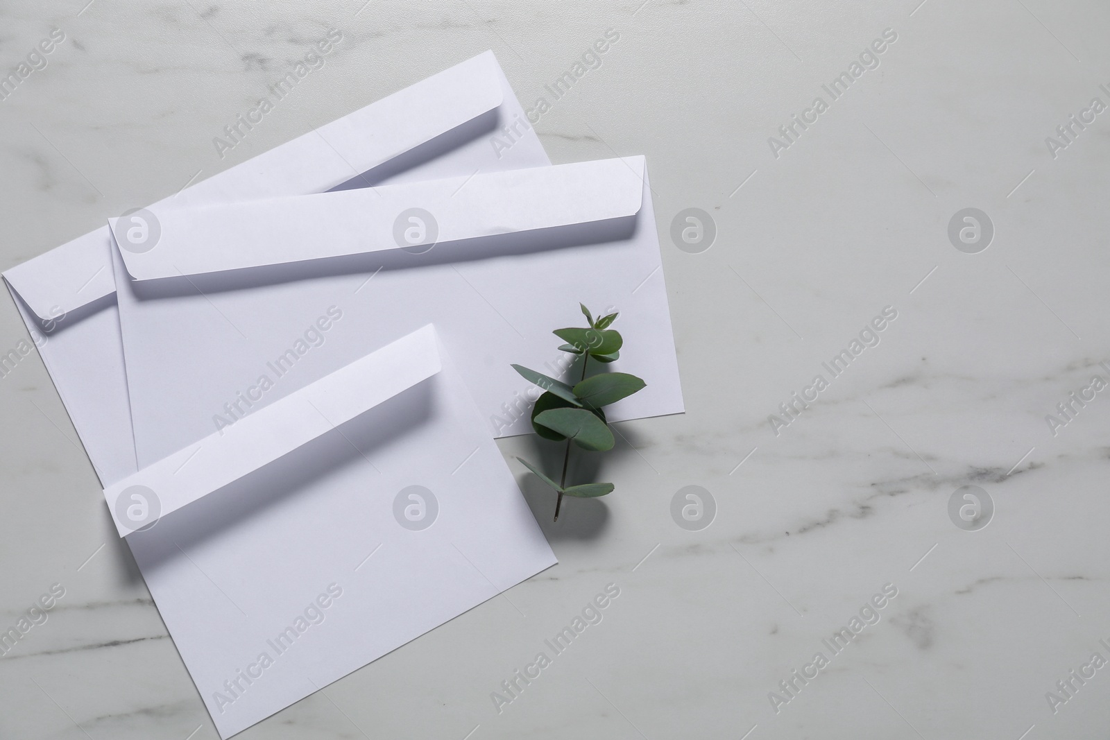 Photo of Paper envelopes and eucalyptus branch on white marble background, flat lay. Mockup for design