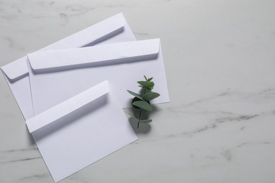 Paper envelopes and eucalyptus branch on white marble background, flat lay. Mockup for design