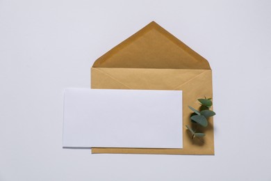 Kraft paper envelope with letter and eucalyptus branch on white background, top view. Mockup for design