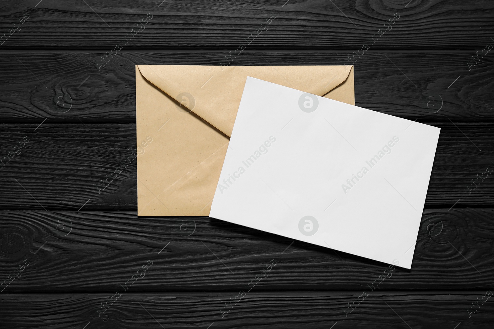 Photo of Kraft paper envelope with letter on black wooden background, top view. Mockup for design