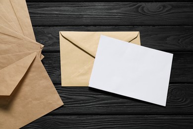 Photo of Kraft paper envelopes with letter on black wooden background, flat lay. Mockup for design