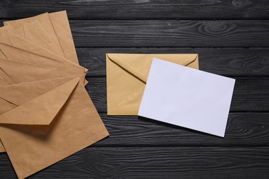 Photo of Kraft paper envelopes with letter on black wooden background, flat lay. Mockup for design