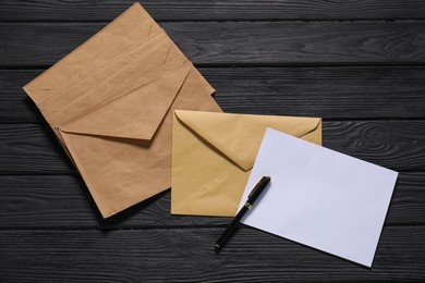 Kraft paper envelopes with letter and pen on black wooden background, flat lay. Mockup for design